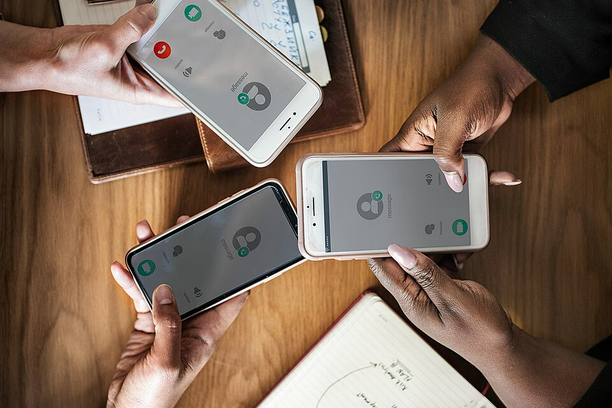 Hands using smartphones during phone calls beside notebooks