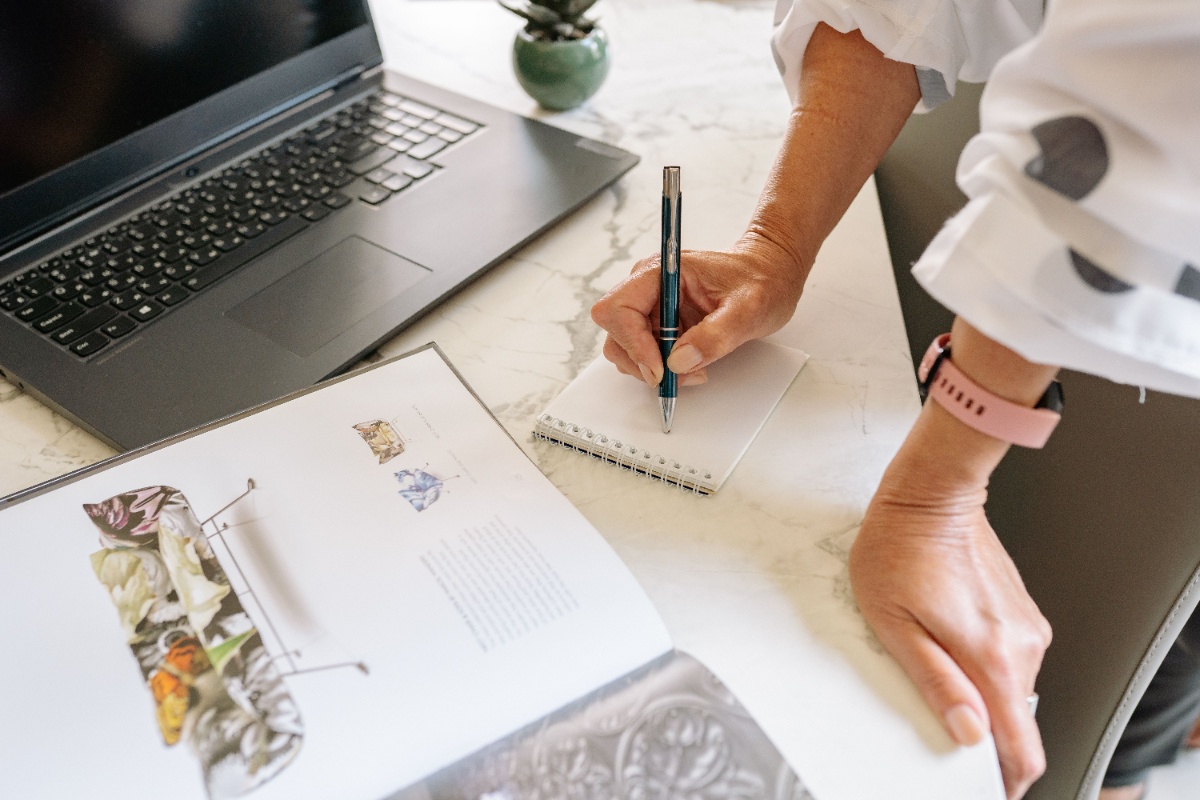 Hands drafting notes beside a laptop before writing an email